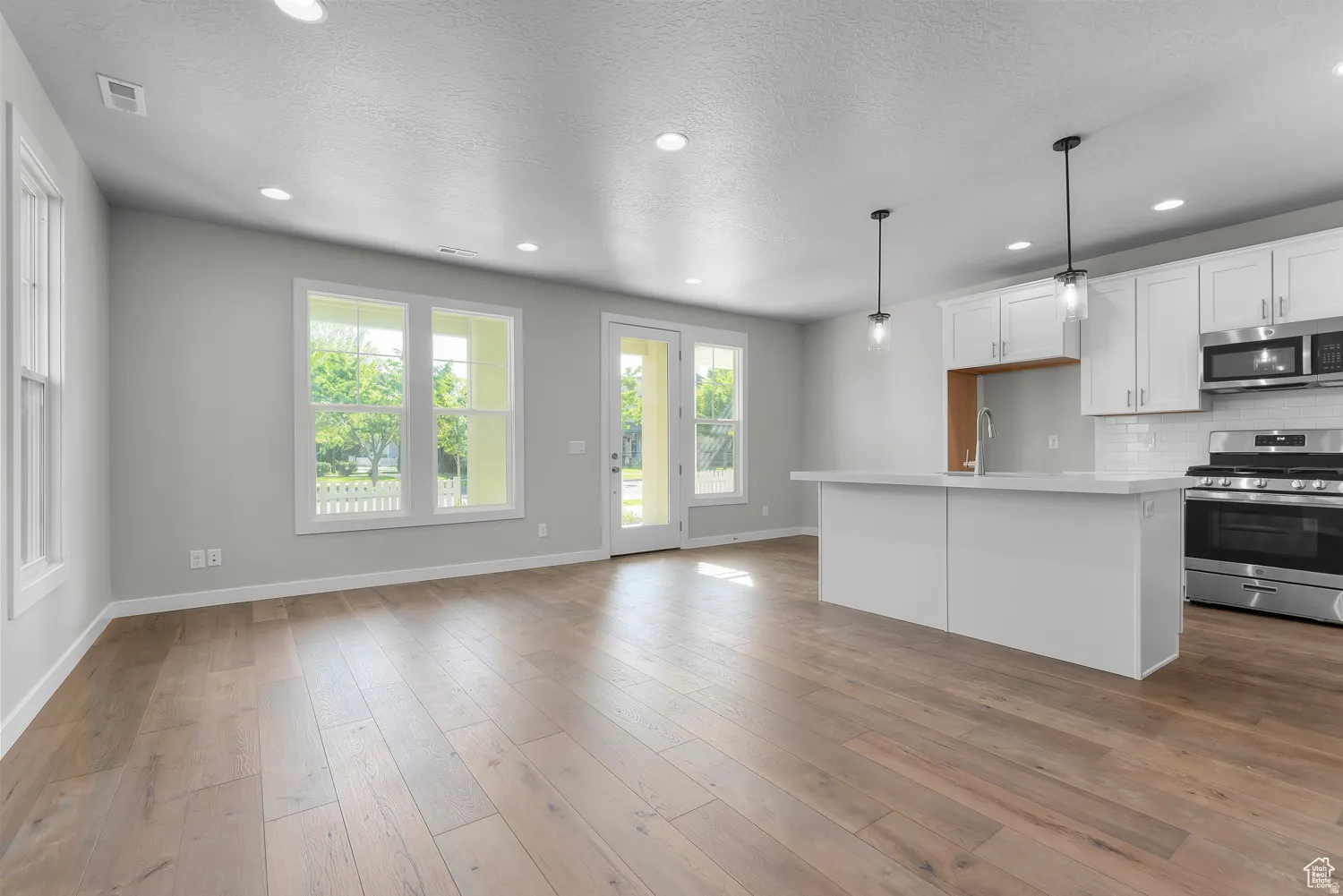 Kitchen with stainless steel appliances, white cabinets, a kitchen island with sink, pendant lighting, and a textured ceiling