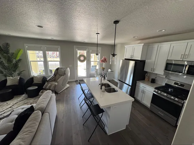 Kitchen featuring open floor plan, a kitchen breakfast bar, stainless steel appliances, dark wood-style floors, and white cabinetry