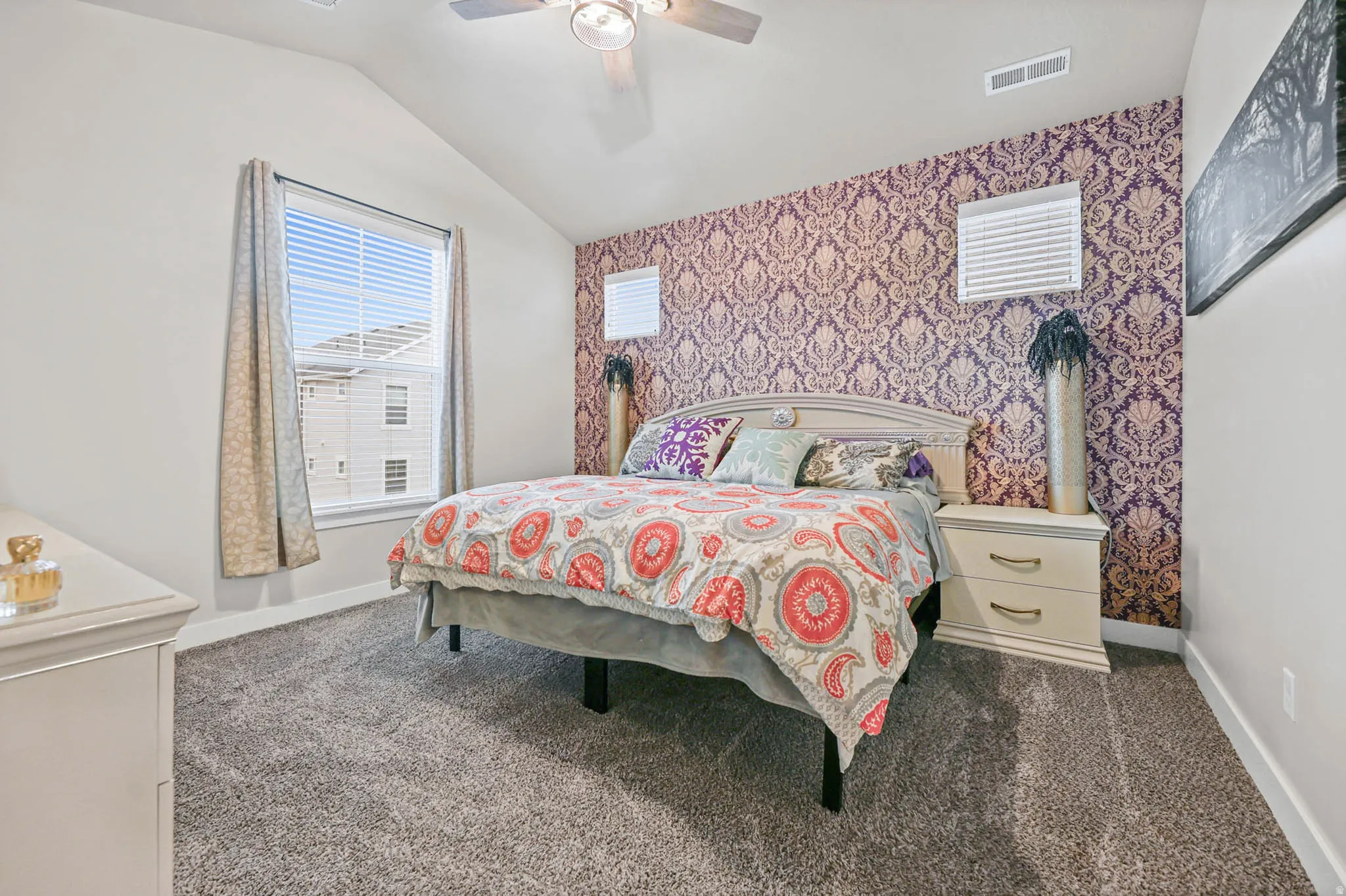 Bedroom with wallpapered walls, ceiling fan, dark carpet, vaulted ceiling, and an accent wall