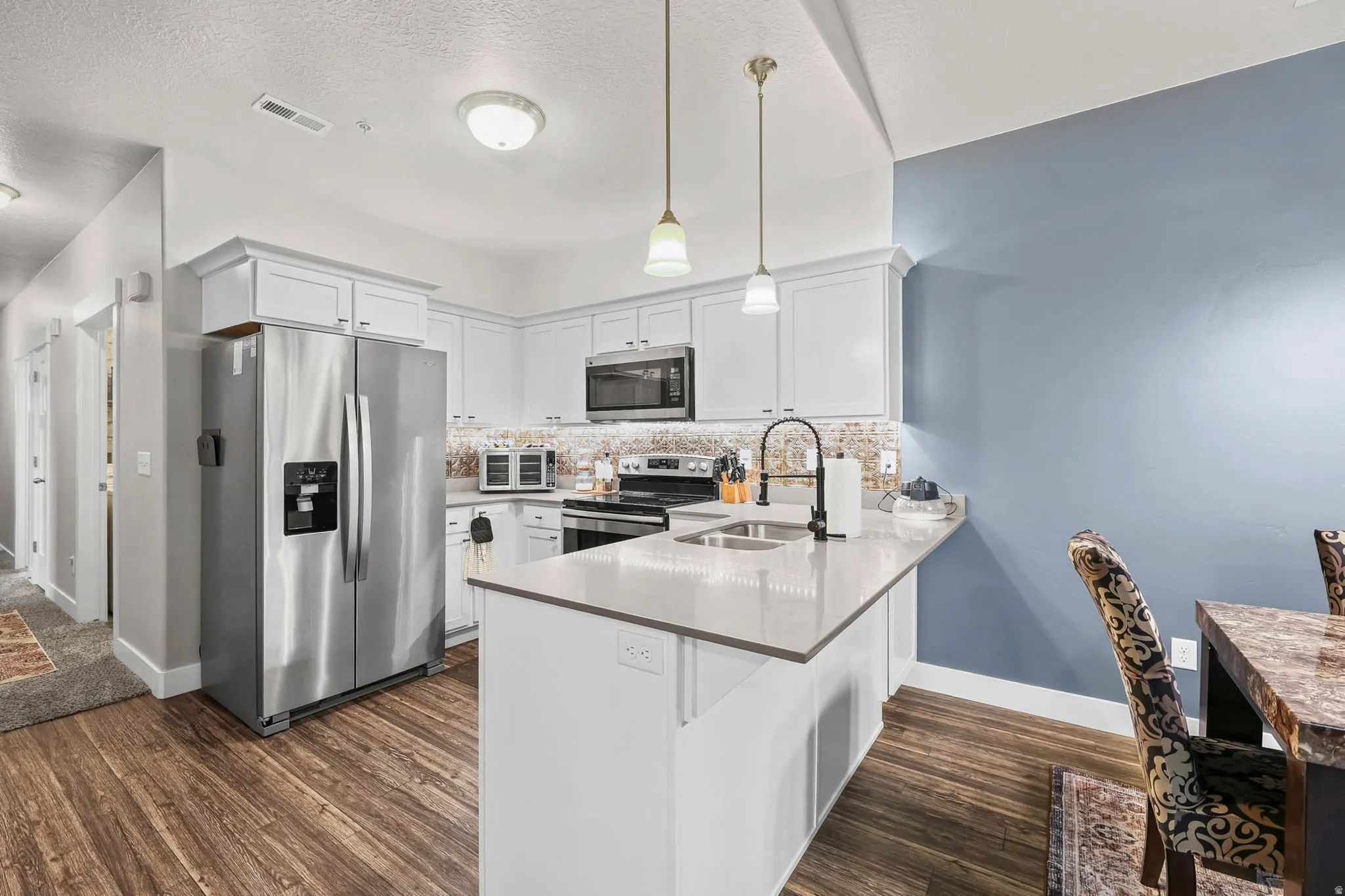 Kitchen featuring stainless steel appliances, a peninsula, white cabinetry, dark wood-style floors, and decorative backsplash