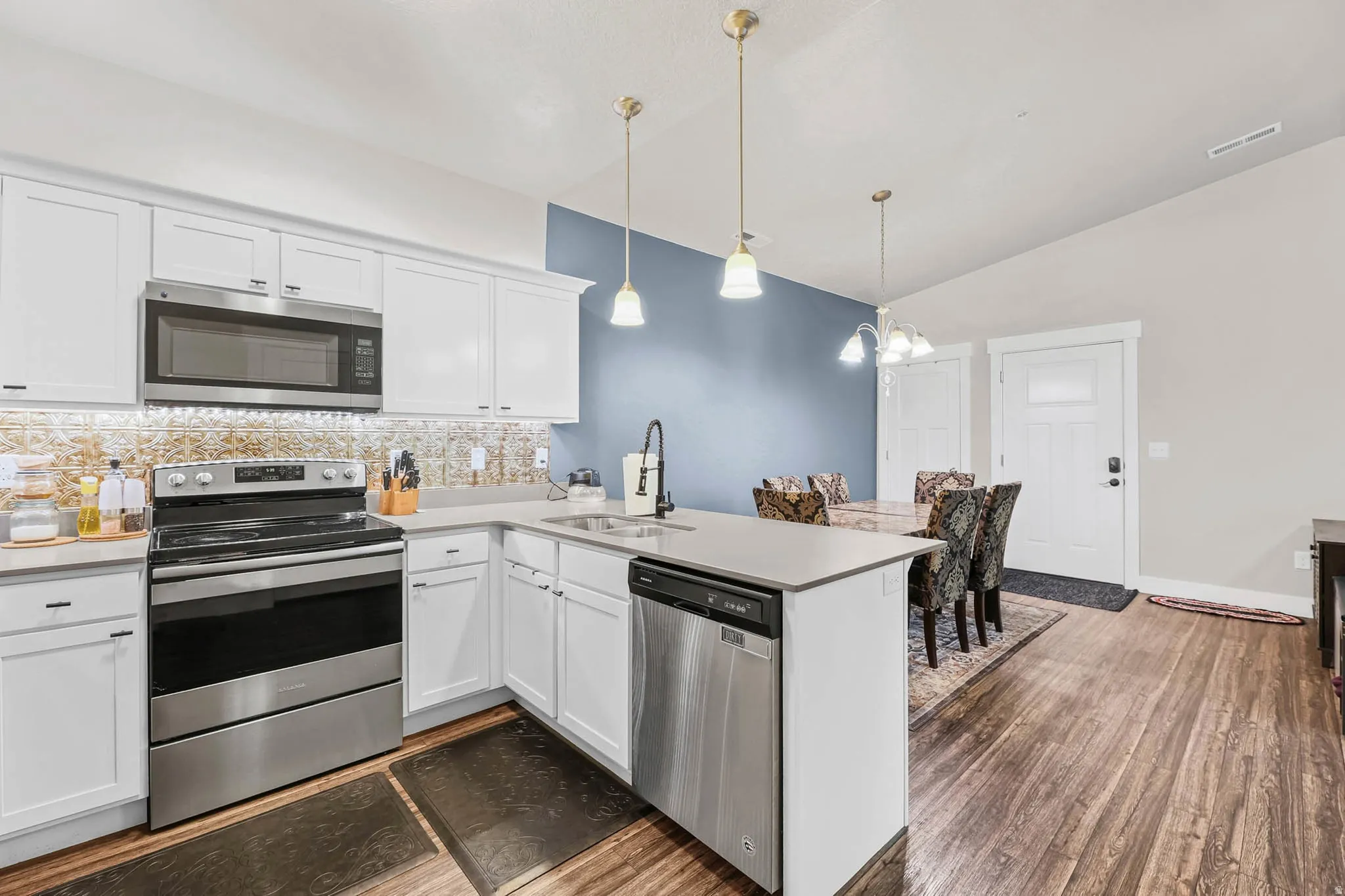 Kitchen featuring stainless steel appliances, a peninsula, decorative backsplash, white cabinets, and light countertops