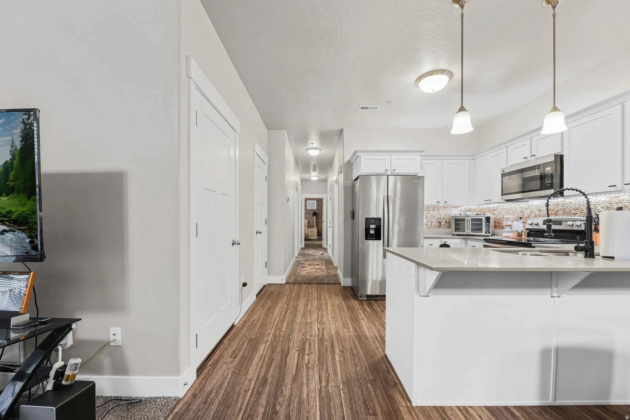Kitchen featuring stainless steel appliances, white cabinets, light stone counters, dark wood-style floors, and a peninsula