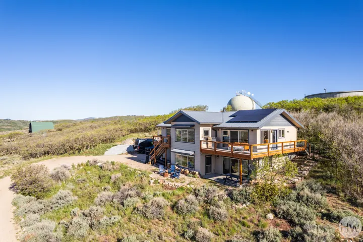 Contemporary multi-level residence featuring a pitched metal roof, solar panels, and a full-width wooden deck