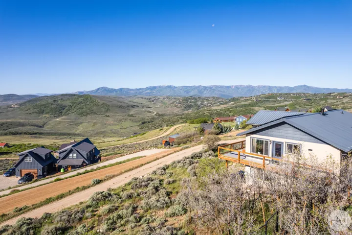 Hillside property featuring a light-colored exterior with a dark-pitched roof and a wooden deck