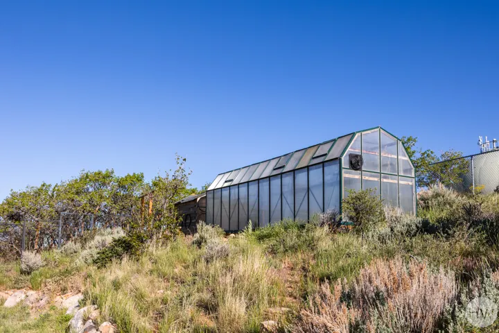 Large, freestanding greenhouse featuring a gabled roof, translucent wall panels, and integrated roof vents