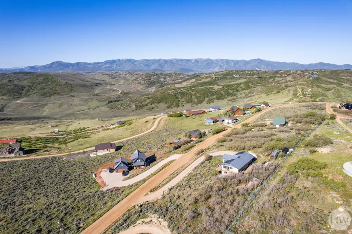 Expansive mountainous landscape featuring scattered residential properties, winding unpaved roads, and distant snow-capped peaks