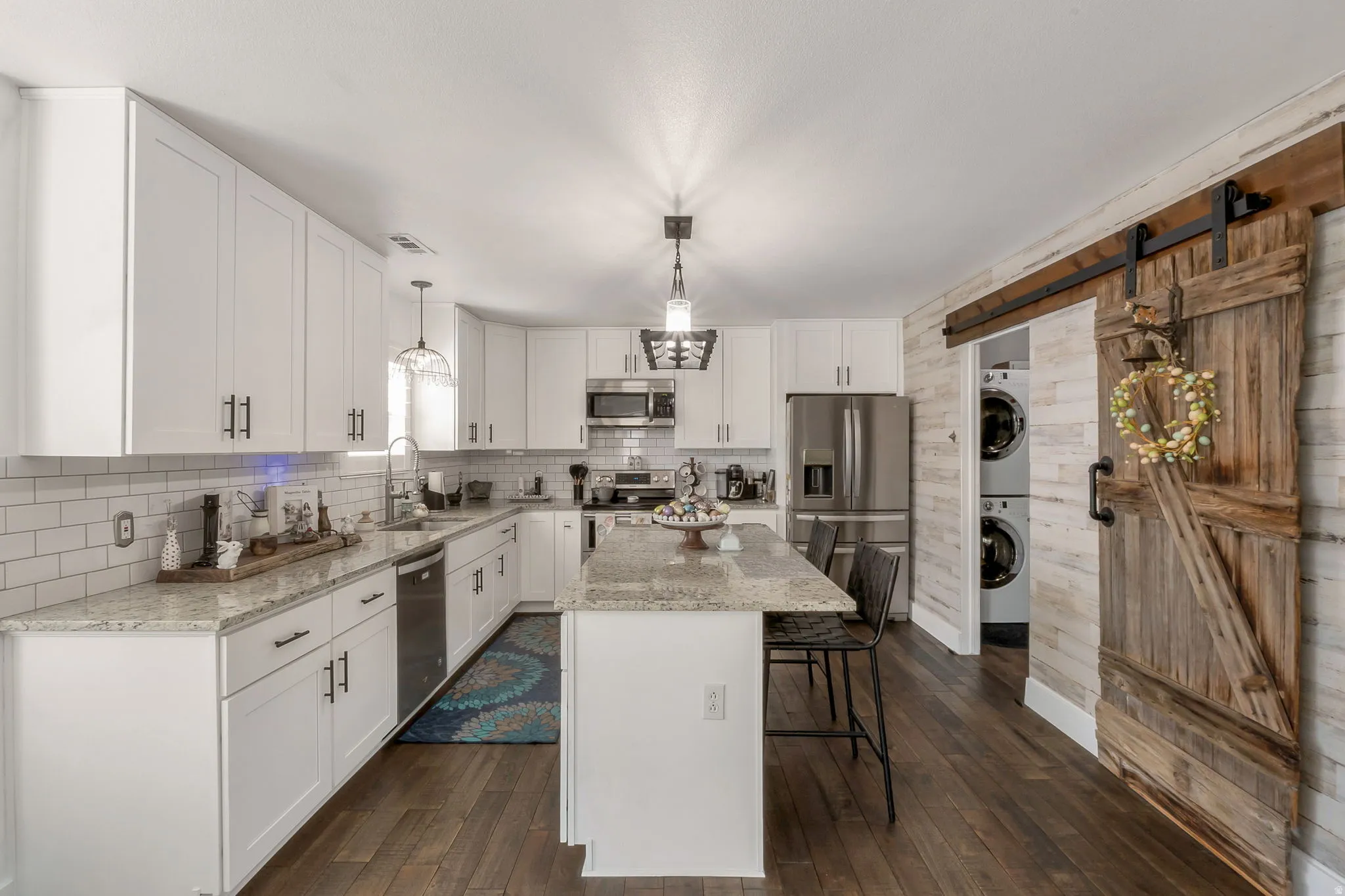 Kitchen featuring a barn door, stainless steel appliances, white cabinets, a kitchen bar, and light stone countertops