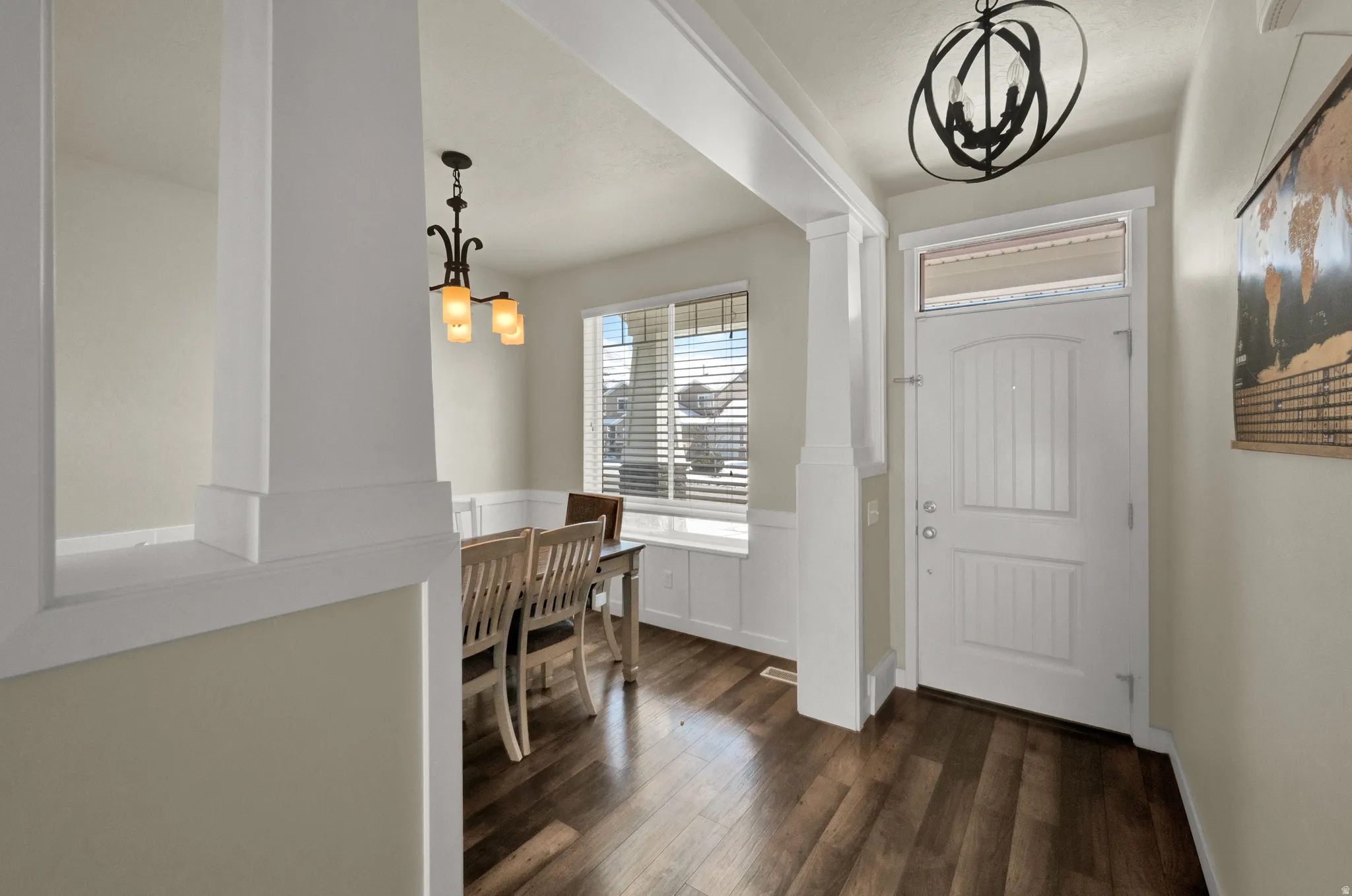 Foyer entrance featuring hanging lights, dark wood finished floors, and a wainscoted wall