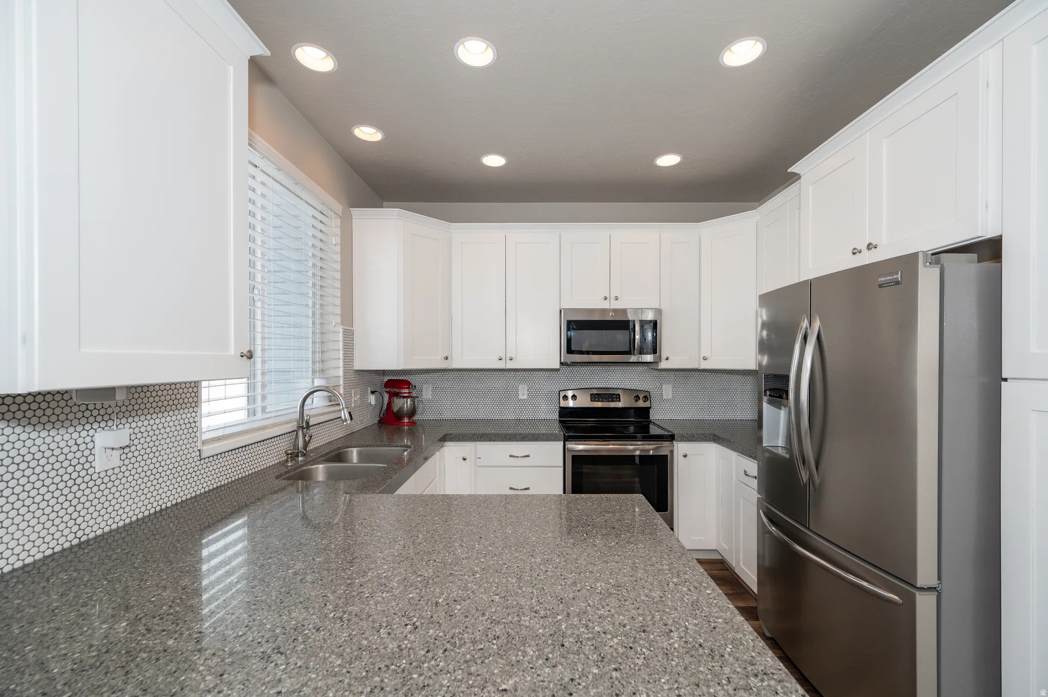 Kitchen with stainless steel appliances, decorative backsplash, white cabinets, dark stone counters, and recessed lighting