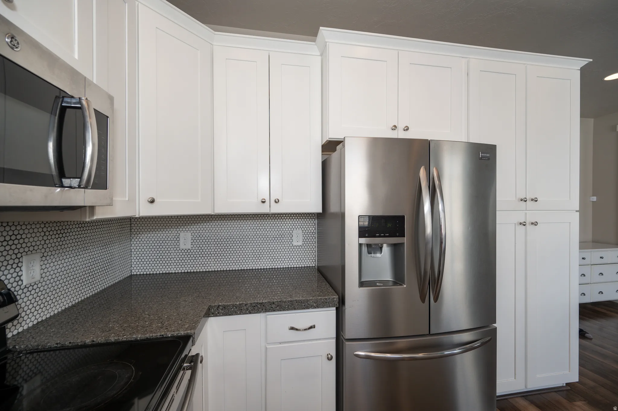 Kitchen with stainless steel appliances, white cabinetry, dark wood-type flooring, dark stone countertops, and decorative backsplash