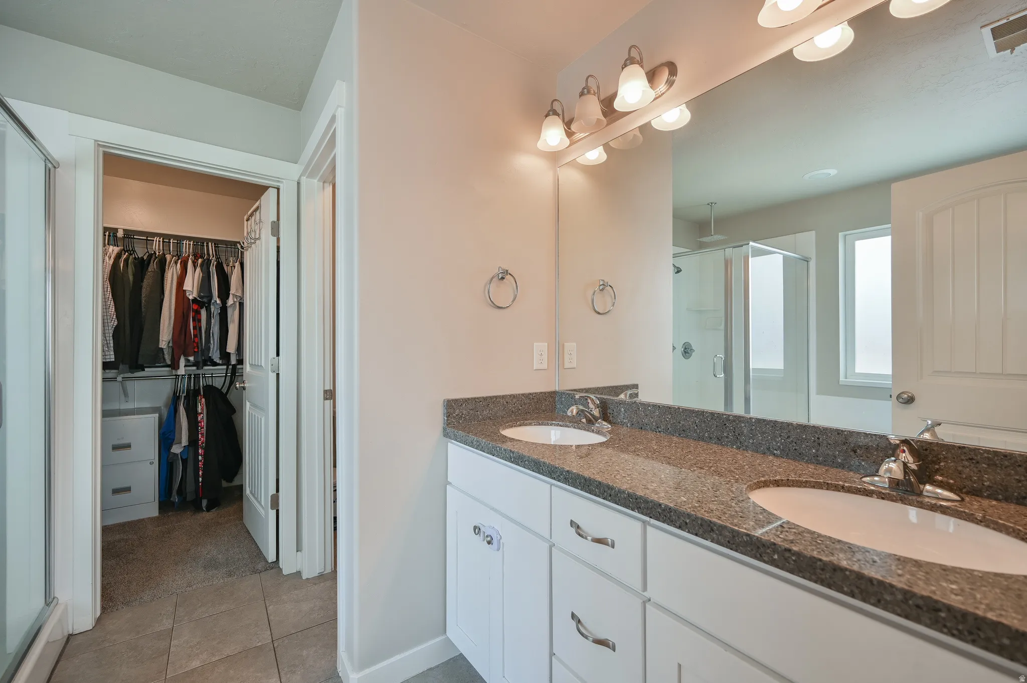 Bathroom with a stall shower, double vanity, a spacious closet, and light tile patterned flooring