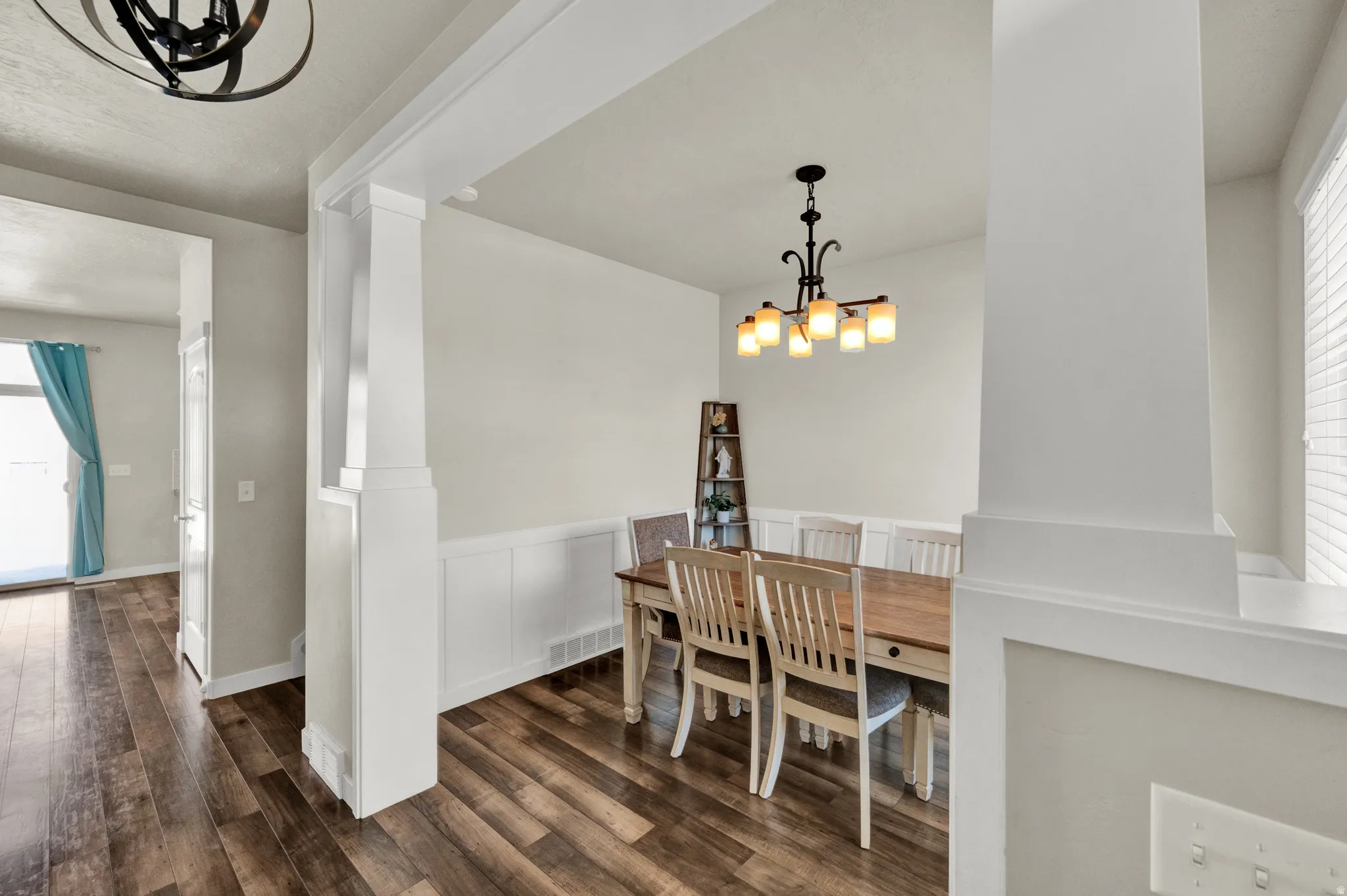 Dining space featuring suspended lighting, dark wood-type flooring, wainscoting, and a decorative wall