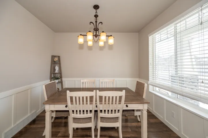 Dining area with a decorative wall, wainscoting, a chandelier, and dark wood-type flooring