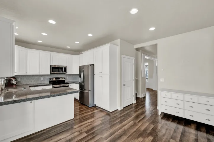 Kitchen featuring dark stone counters, white cabinetry, stainless steel appliances, a peninsula, and dark wood-style flooring
