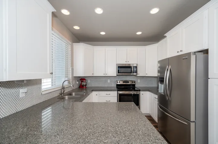 Kitchen with stainless steel appliances, decorative backsplash, white cabinets, dark stone counters, and recessed lighting