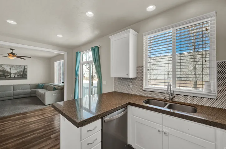 Kitchen with white cabinetry, tasteful backsplash, stainless steel dishwasher, dark wood-style floors, and open floor plan