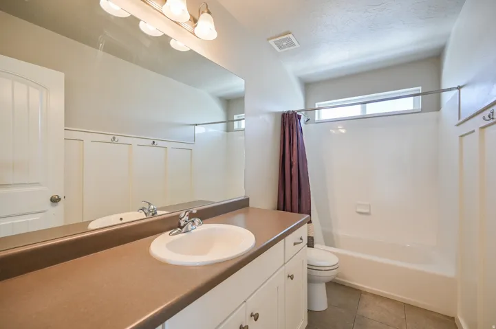 Bathroom featuring vanity, shower / tub combo with curtain, light tile patterned flooring, a textured ceiling, and a decorative wall