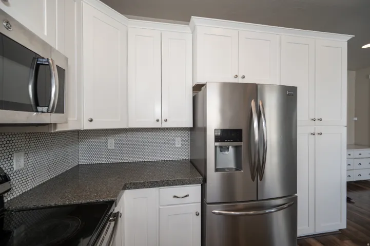 Kitchen with stainless steel appliances, white cabinetry, dark wood-type flooring, dark stone countertops, and decorative backsplash