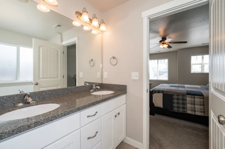 Ensuite bathroom featuring double vanity, a ceiling fan, and dark colored carpet