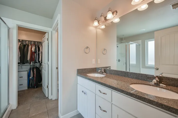 Bathroom with a stall shower, double vanity, a spacious closet, and light tile patterned flooring