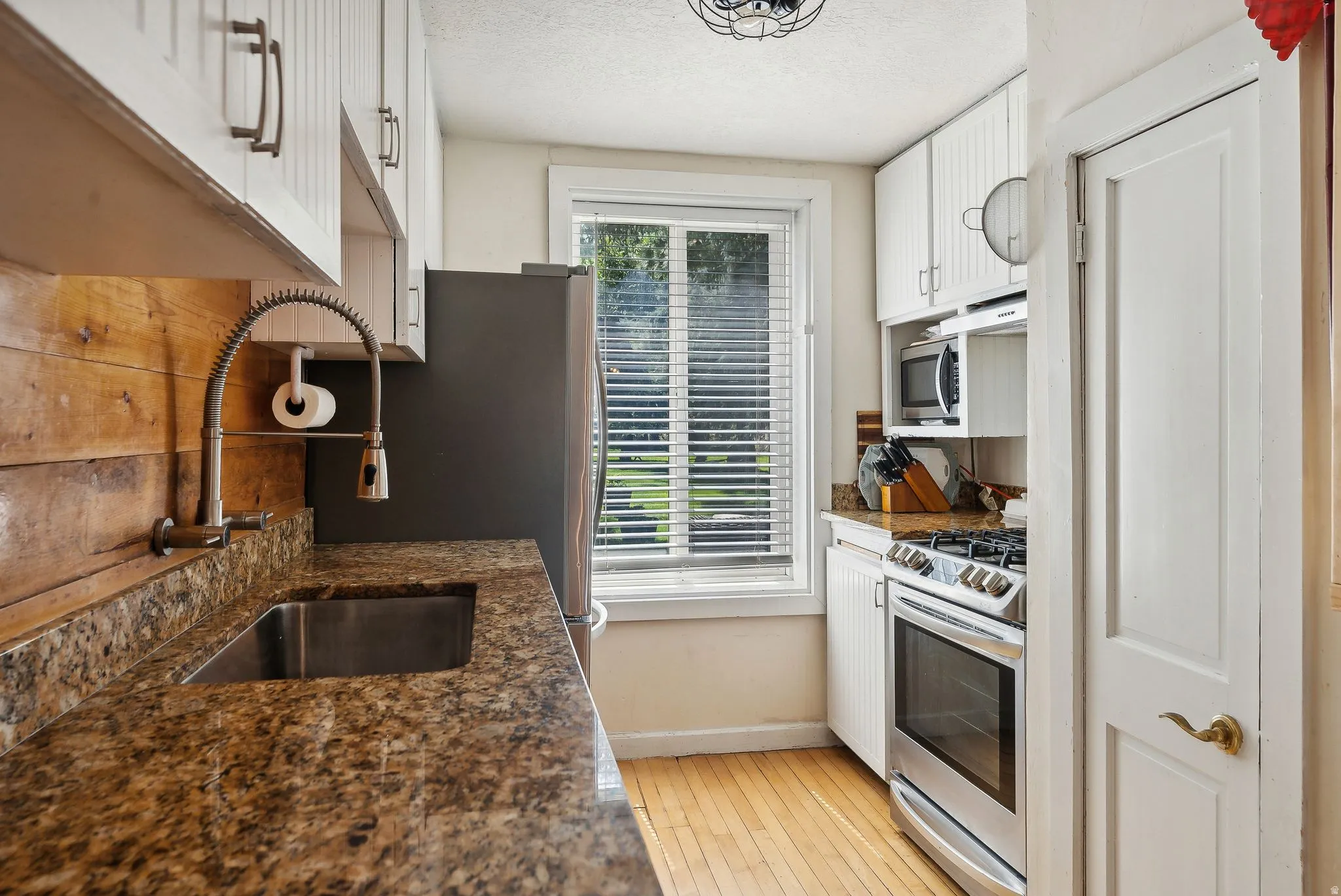 Kitchen featuring white cabinets, dark stone counters, stainless steel appliances, light wood-style flooring, and a textured ceiling
