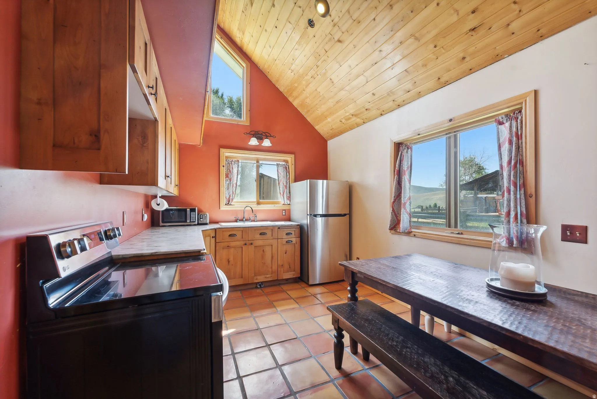 Kitchen featuring stainless steel appliances, a vaulted wooden ceiling, light countertops, wood finish cabinetry, and light tile patterned floors