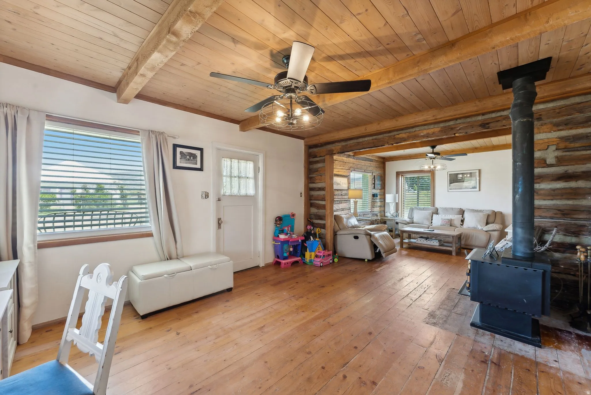Living room featuring a wood stove, a wood ceiling with exposed beams, light wood-style flooring, and a ceiling fan