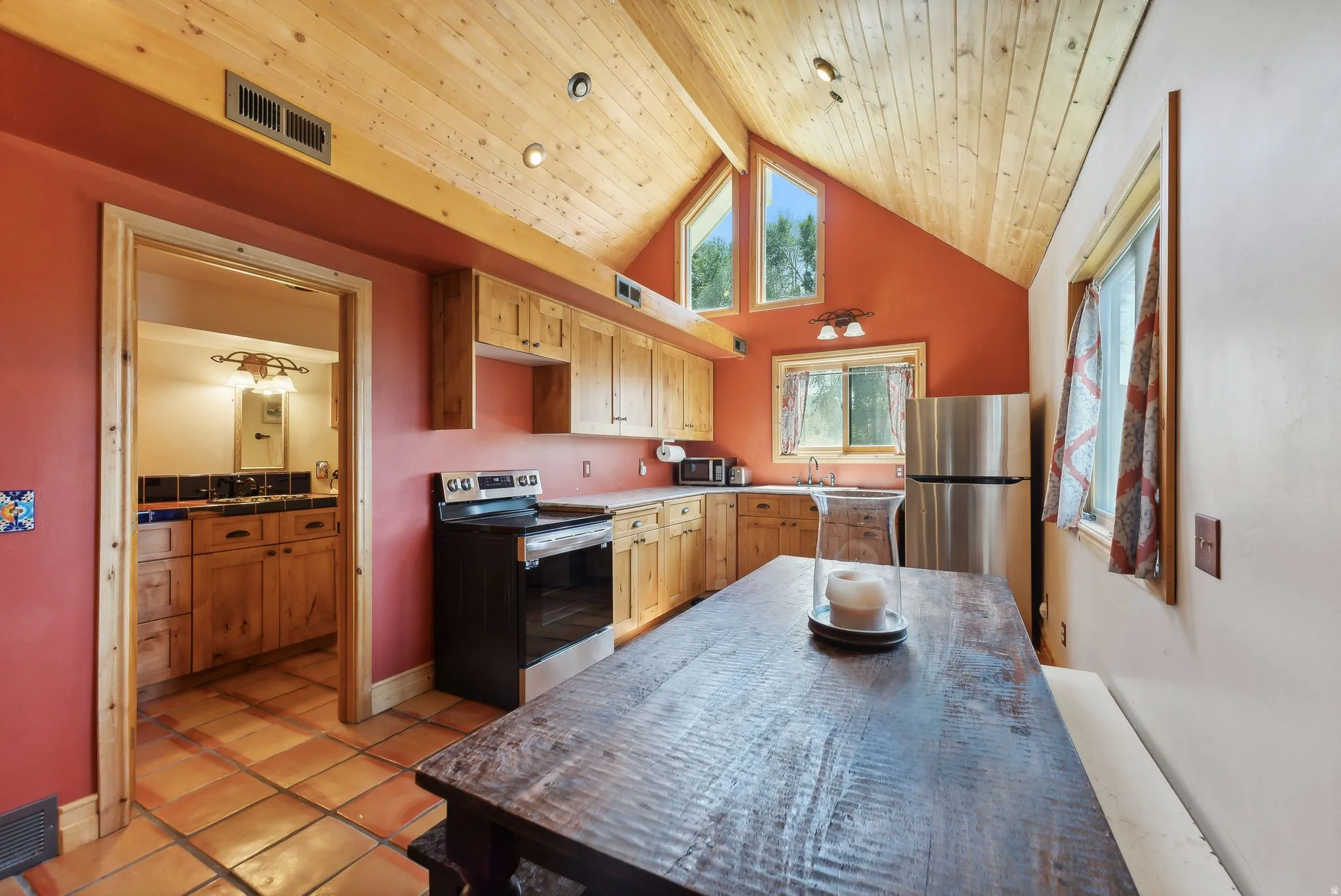 Kitchen featuring stainless steel appliances, light wood finish cabinetry, a high wooden beamed ceiling, light tile patterned flooring, and light countertops