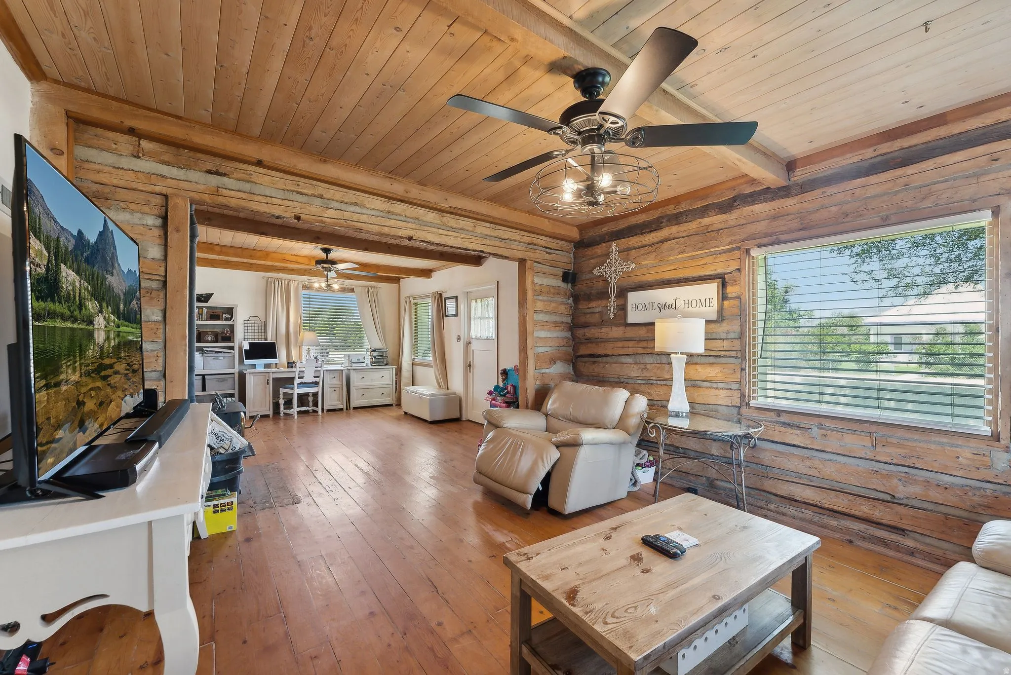 Living room featuring a wooden ceiling with exposed beams, a ceiling fan, wood-type flooring, and log walls