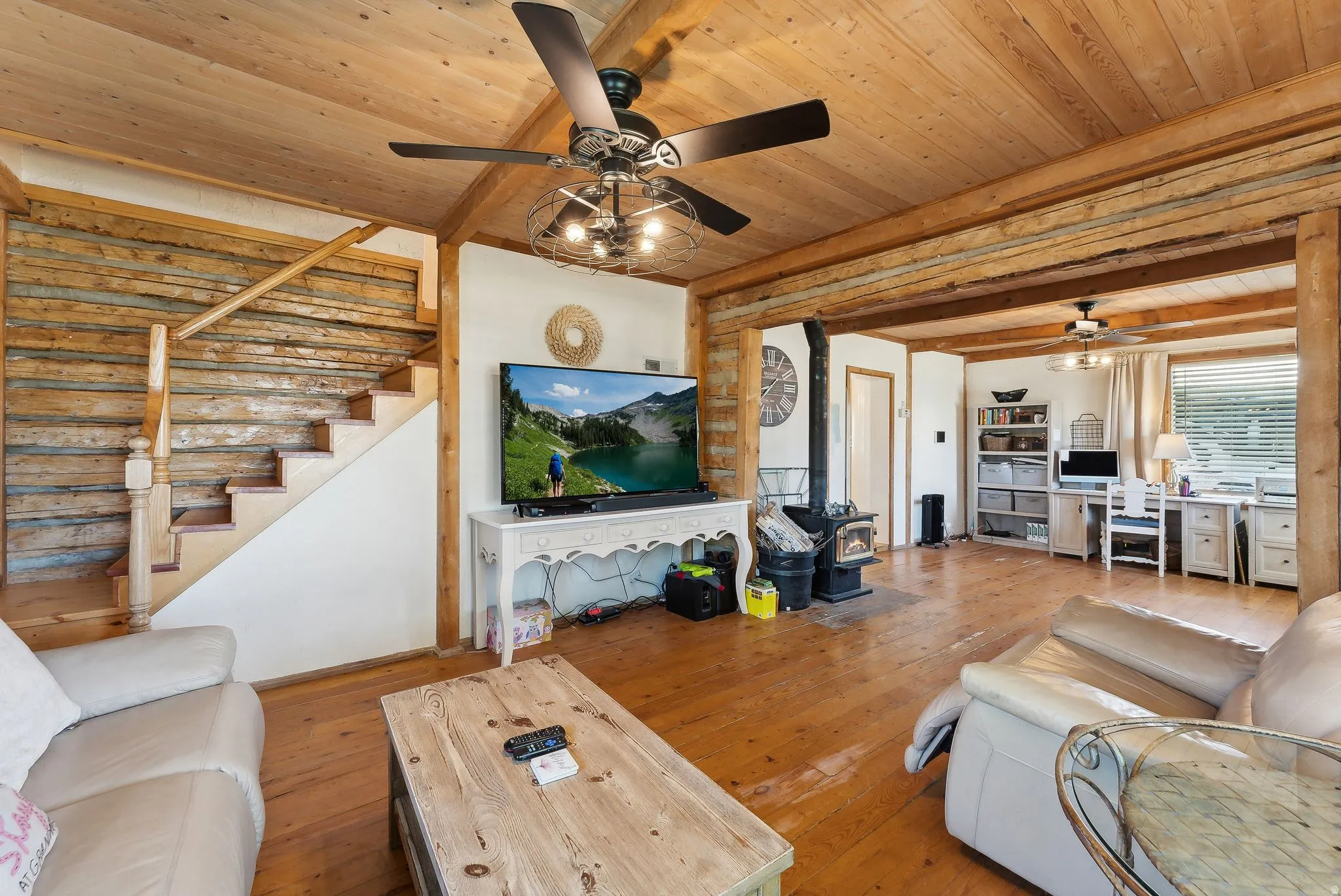 Living room featuring ceiling fan, a wood stove, wood-type flooring, and a wood ceiling with exposed beams