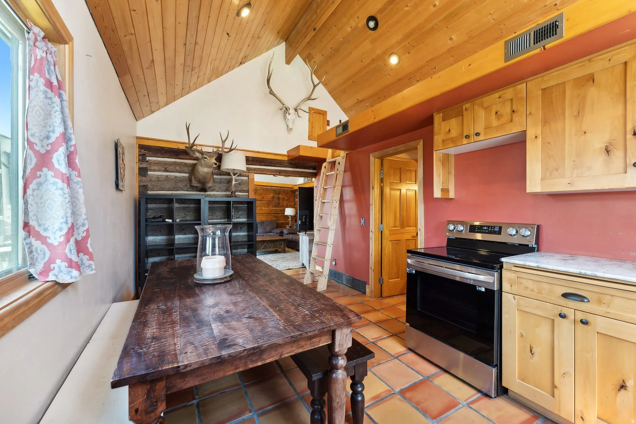 Kitchen with electric range, light wood finish cabinets, light tile patterned flooring, and a high wood beamed ceiling