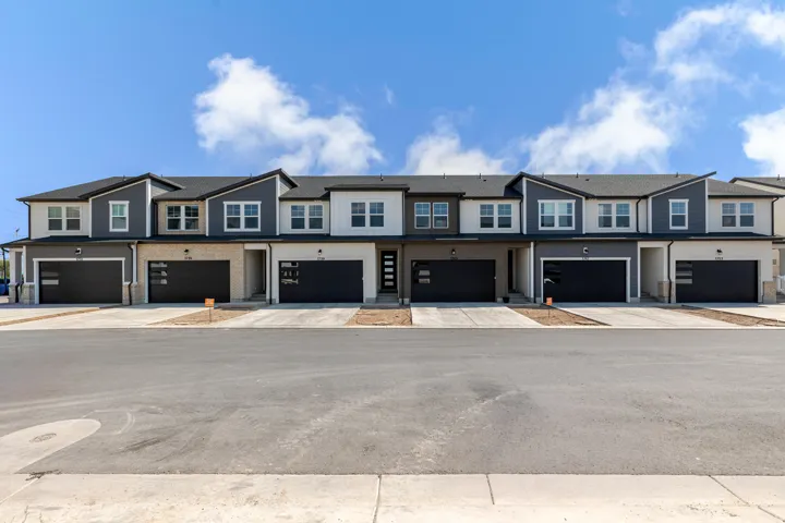 Modern townhome facade featuring multi-tone siding, dark garage doors with frosted glass panels, and a well-maintained asphalt driveway