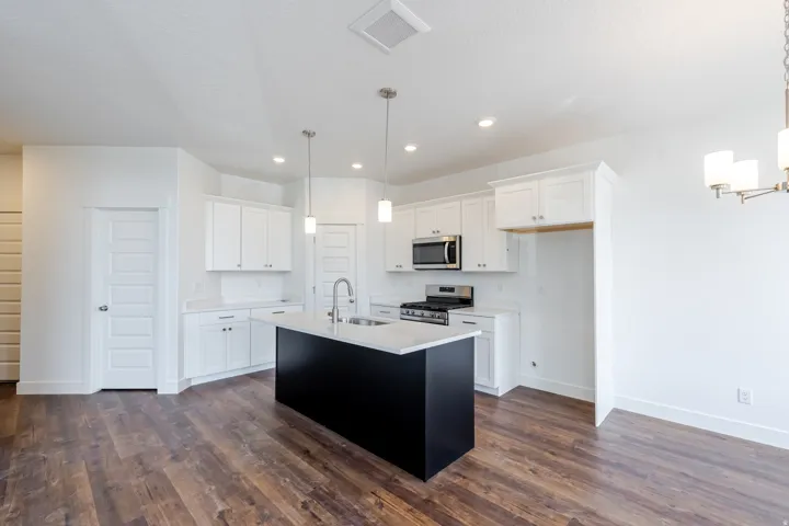 Kitchen featuring white cabinetry, a dark-toned island with a light-toned countertop, stainless steel appliances, and wood-finish flooring