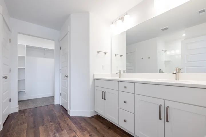 Dual vanity with white cabinetry, wood-finish flooring, a large mirror, and brushed nickel hardware