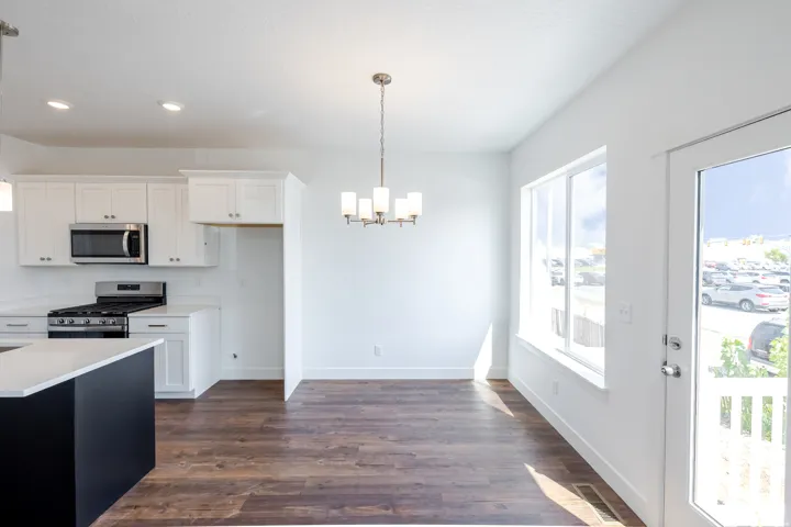 Kitchen and dining area featuring white cabinetry, stainless steel appliances, a center island with a light-toned countertop, wood-finish flooring, and a large window