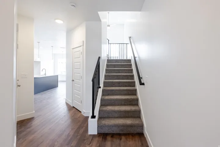 Carpeted staircase with black metal railing, wood-finish flooring, white panel doors, and recessed lighting