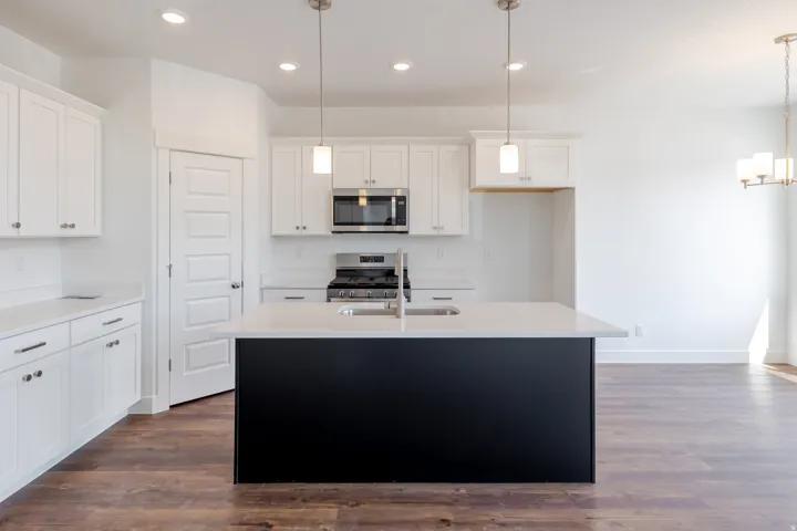 Modern kitchen featuring white cabinetry, a dark-toned island with an undermount sink, stainless steel appliances, and recessed lighting