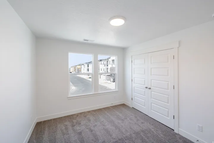 Neutral wall paint, plush carpet flooring, dual windows, flush mount ceiling light, and bi-fold closet doors