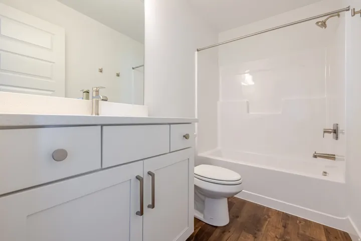 White vanity with a light-toned countertop, brushed nickel faucet, wood-finish flooring, and a white tub/shower combination