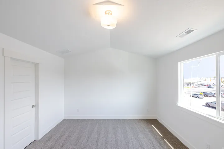 Vaulted ceiling with an attached light fixture, white interior door with contemporary hardware, large window, and gray carpet