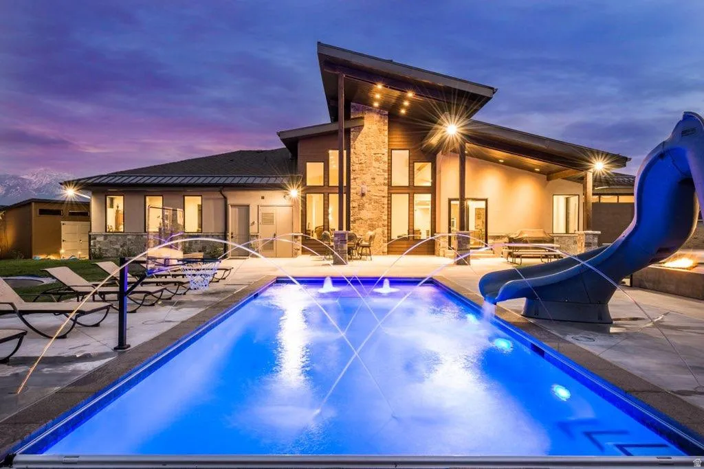 Back of house at dusk featuring a patio, stone siding, stucco siding, a standing seam roof, and an outdoor pool