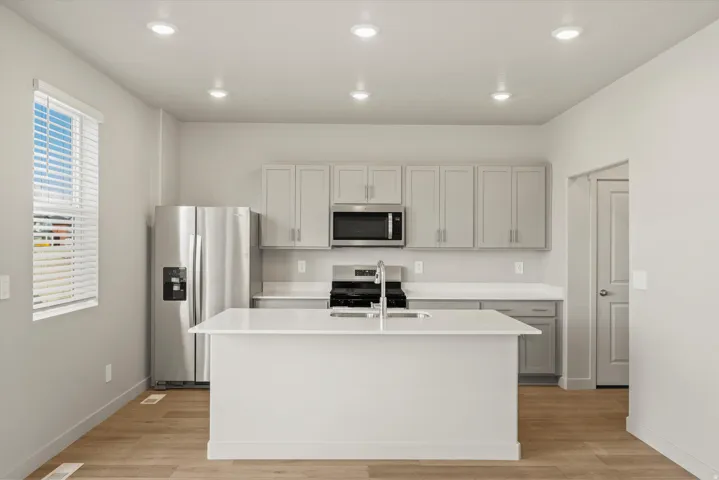 Kitchen with stainless steel appliances, light wood finished floors, recessed lighting, a center island with sink, and gray cabinetry