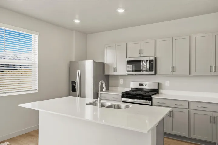 Kitchen with stainless steel appliances, a kitchen island with sink, light wood finished floors, light stone countertops, and recessed lighting