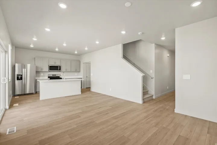 Kitchen with stainless steel appliances, light countertops, an island with sink, open floor plan, and light wood finished floors