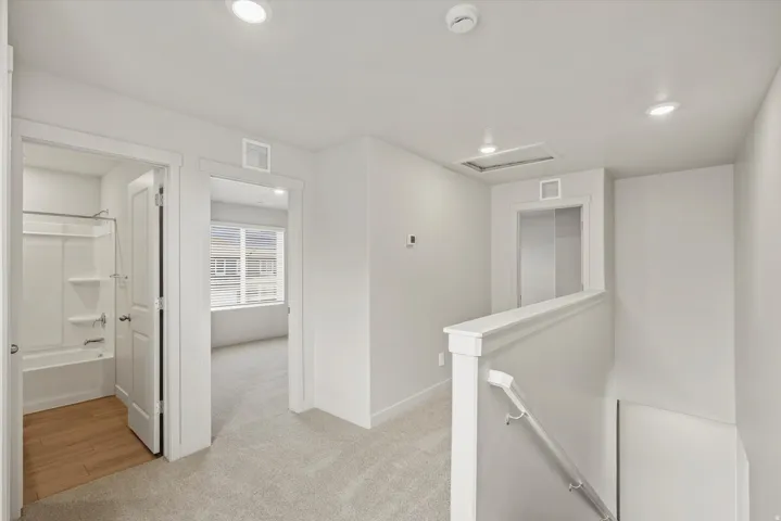 Hall with an upstairs landing, light colored carpet, and recessed lighting