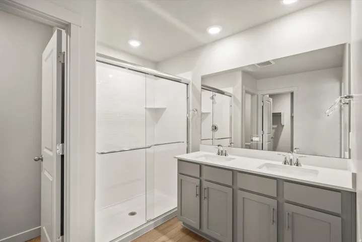 Bathroom with double vanity, a stall shower, light wood-style flooring, and recessed lighting