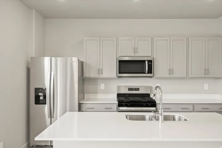 Kitchen with stainless steel appliances, an island with sink, light stone counters, and white cabinetry
