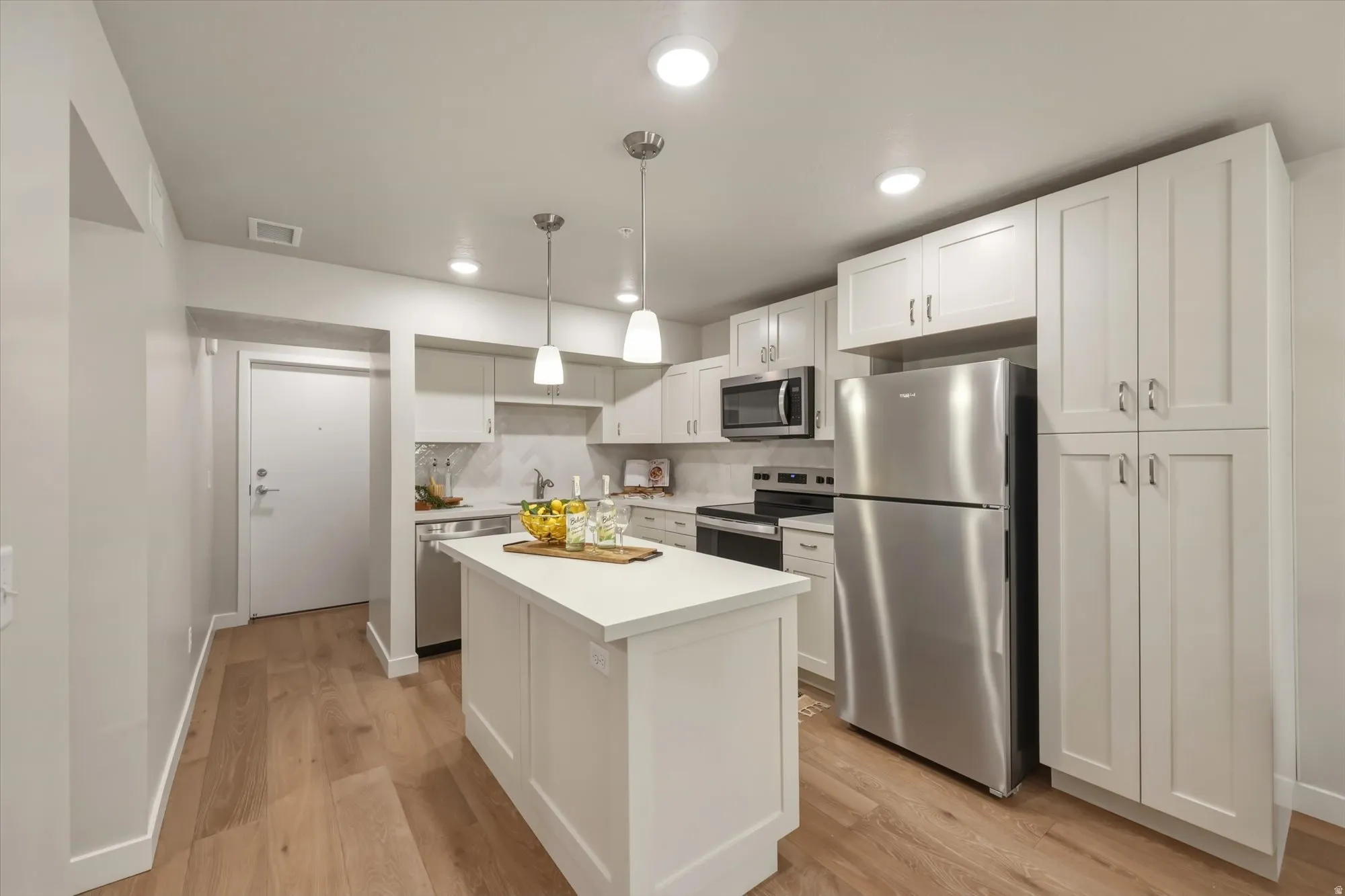 Kitchen with stainless steel appliances, white cabinets, light countertops, light wood-style flooring, and hanging light fixtures