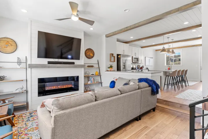 Living room featuring ceiling fan, a large fireplace, light wood-style floors, beamed ceiling, and recessed lighting