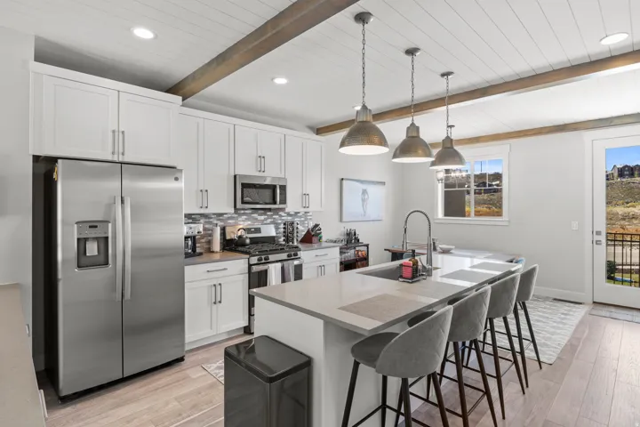 Kitchen with stainless steel appliances, an island with sink, a breakfast bar area, pendant lighting, and white cabinets